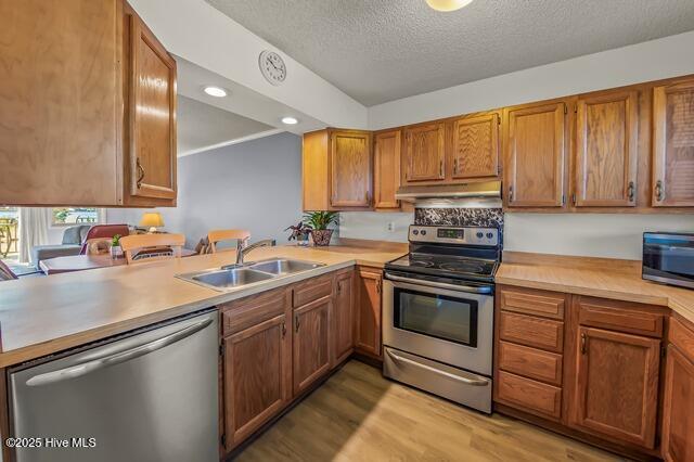 kitchen with sink, stainless steel appliances, kitchen peninsula, light hardwood / wood-style floors, and a textured ceiling