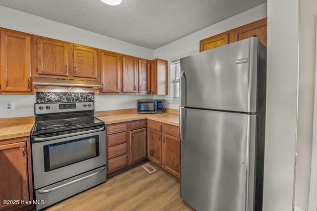 kitchen with a textured ceiling, light wood-type flooring, and stainless steel appliances