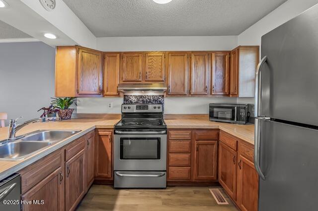 kitchen featuring a textured ceiling, light wood-type flooring, sink, and appliances with stainless steel finishes