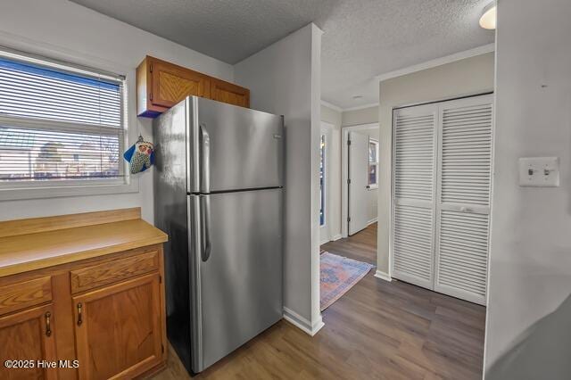 kitchen with stainless steel fridge, a textured ceiling, light hardwood / wood-style floors, and crown molding