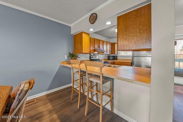 kitchen featuring dark hardwood / wood-style floors, a textured ceiling, a kitchen bar, kitchen peninsula, and stainless steel appliances