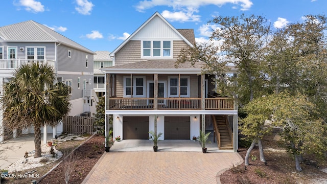 raised beach house with a garage, stairway, roof with shingles, decorative driveway, and board and batten siding