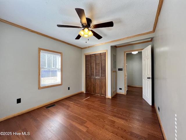 unfurnished bedroom featuring ceiling fan, dark wood-type flooring, a textured ceiling, a closet, and ornamental molding