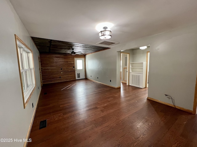 unfurnished room featuring dark hardwood / wood-style flooring, ceiling fan, and wooden walls