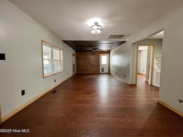 unfurnished room with ceiling fan, dark wood-type flooring, and wood walls