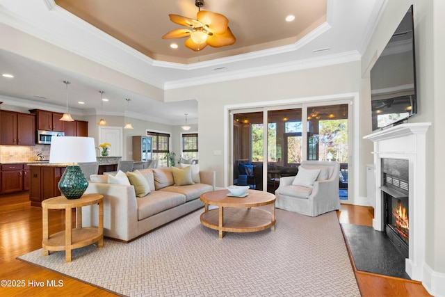 living room featuring ceiling fan, light hardwood / wood-style floors, a tray ceiling, and crown molding