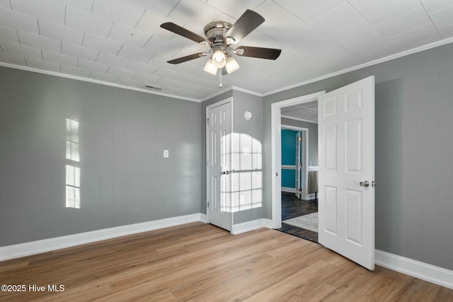 spare room with light wood finished floors, a ceiling fan, baseboards, and crown molding