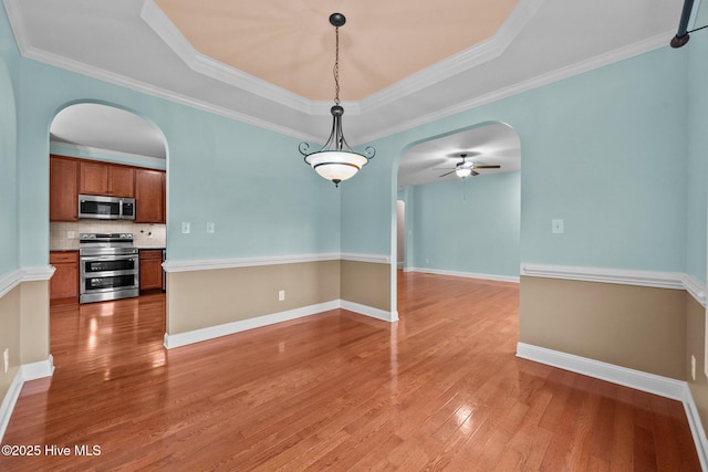 empty room with a tray ceiling, ceiling fan, wood-type flooring, and ornamental molding