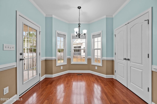 unfurnished dining area with hardwood / wood-style floors, a notable chandelier, and crown molding