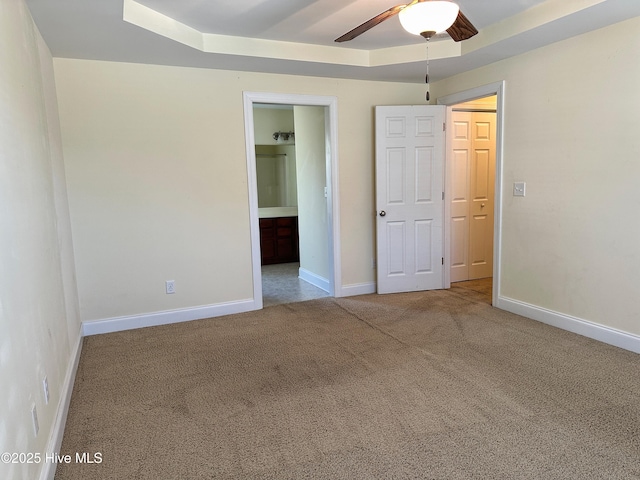 unfurnished bedroom featuring a tray ceiling, ensuite bath, ceiling fan, and carpet