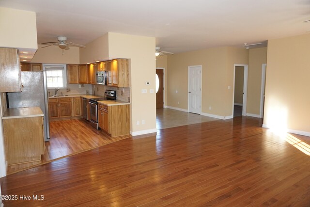 kitchen with appliances with stainless steel finishes, tasteful backsplash, ceiling fan, sink, and light hardwood / wood-style flooring