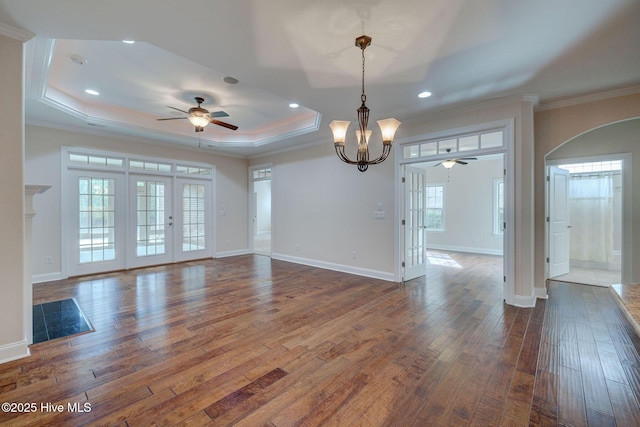 spare room with ceiling fan with notable chandelier, a raised ceiling, crown molding, and dark wood-type flooring