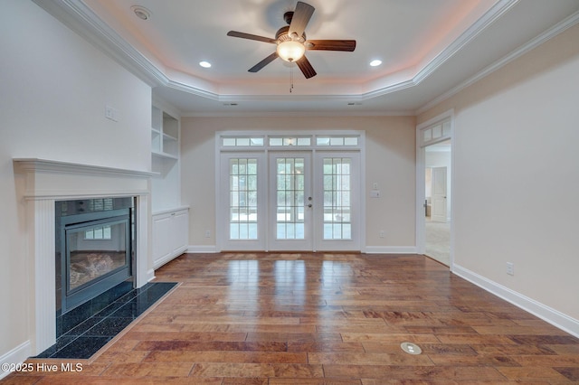 unfurnished living room with a tray ceiling, a tile fireplace, ceiling fan, and hardwood / wood-style flooring