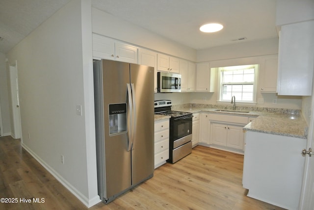 kitchen featuring sink, light hardwood / wood-style flooring, stainless steel appliances, light stone countertops, and white cabinets