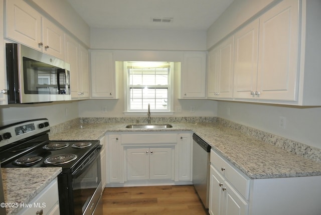 kitchen with sink, white cabinetry, light stone counters, light hardwood / wood-style flooring, and appliances with stainless steel finishes