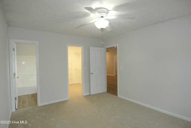 unfurnished bedroom with a spacious closet, light carpet, a textured ceiling, a closet, and ceiling fan