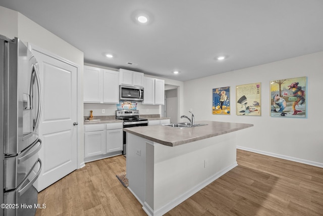 kitchen featuring appliances with stainless steel finishes, sink, light hardwood / wood-style floors, white cabinetry, and an island with sink