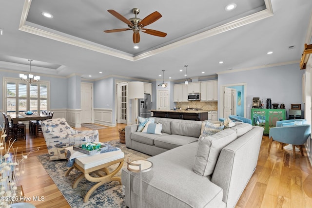 living room featuring ceiling fan with notable chandelier, a raised ceiling, light wood-type flooring, and crown molding