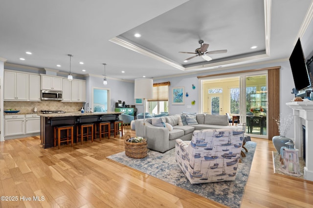 living room with ceiling fan, sink, a raised ceiling, light hardwood / wood-style floors, and ornamental molding