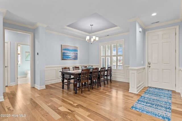 dining area featuring a raised ceiling, a chandelier, light wood-type flooring, and ornamental molding