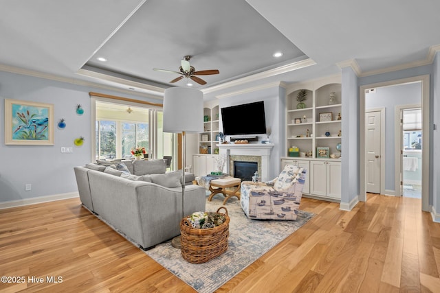 living room featuring a tray ceiling, built in features, light hardwood / wood-style floors, and crown molding