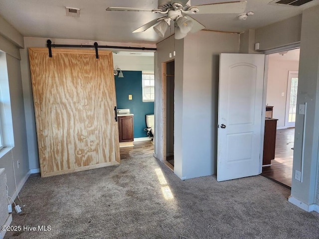 unfurnished bedroom with a barn door, ceiling fan, and carpet floors