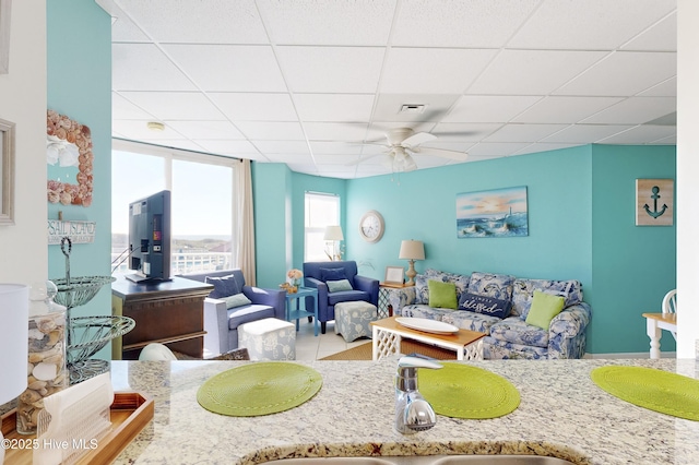 living room featuring ceiling fan, a drop ceiling, and sink