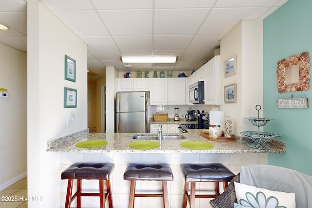 kitchen featuring white cabinetry, sink, kitchen peninsula, stainless steel fridge, and light tile patterned flooring