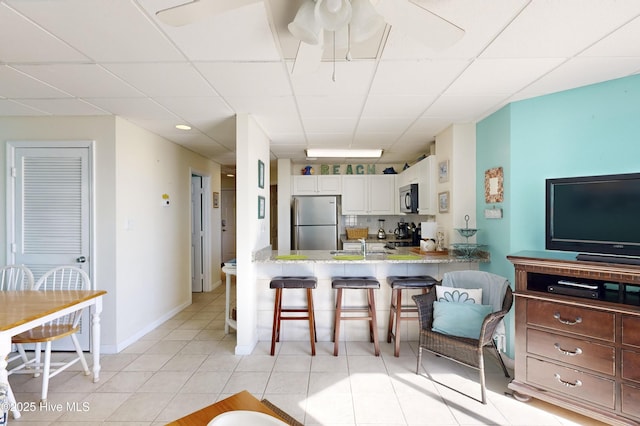 kitchen with stainless steel refrigerator, white cabinetry, kitchen peninsula, a breakfast bar area, and a paneled ceiling