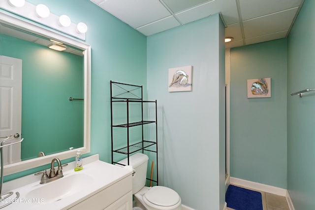 bathroom with tile patterned flooring, a drop ceiling, vanity, and toilet