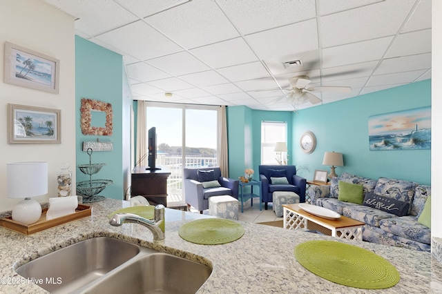 kitchen featuring a drop ceiling, sink, ceiling fan, light stone countertops, and light tile patterned floors