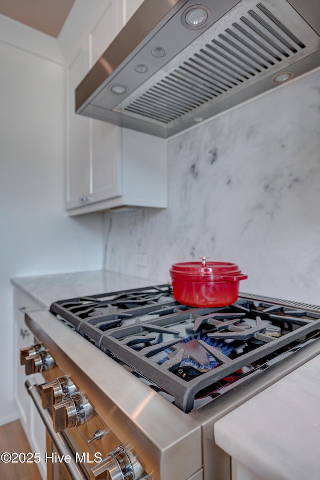 kitchen with white cabinets, wood-type flooring, high end stainless steel range, and wall chimney exhaust hood