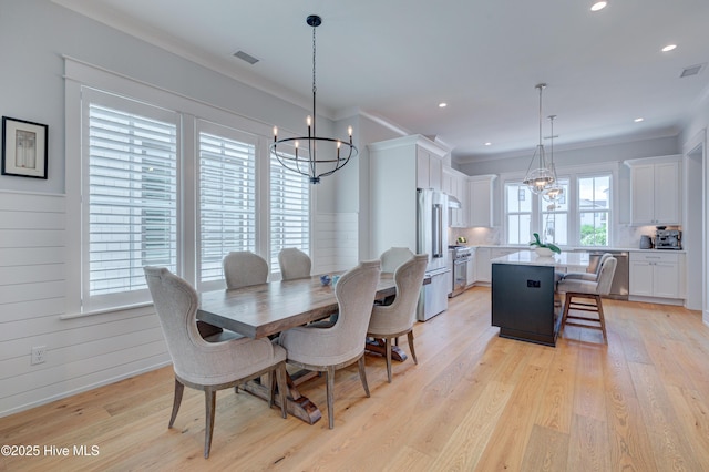 dining area with a notable chandelier, crown molding, and light hardwood / wood-style flooring