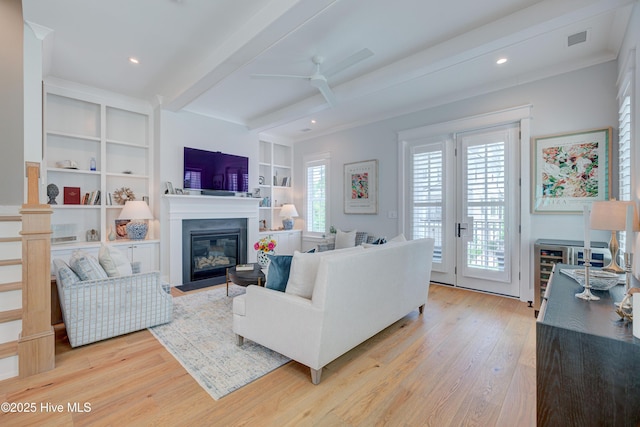 living room with beamed ceiling, built in shelves, ceiling fan, and light hardwood / wood-style flooring