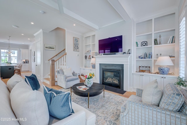 living room with crown molding, built in shelves, light hardwood / wood-style floors, and beamed ceiling