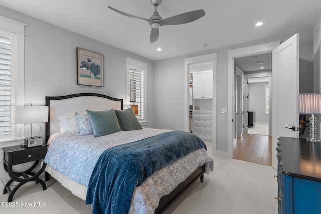 bedroom with ceiling fan, light colored carpet, and a walk in closet