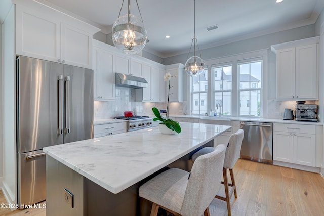 kitchen with appliances with stainless steel finishes, white cabinetry, a kitchen island, decorative backsplash, and decorative light fixtures