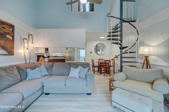 living room featuring ceiling fan, light wood-type flooring, and a towering ceiling