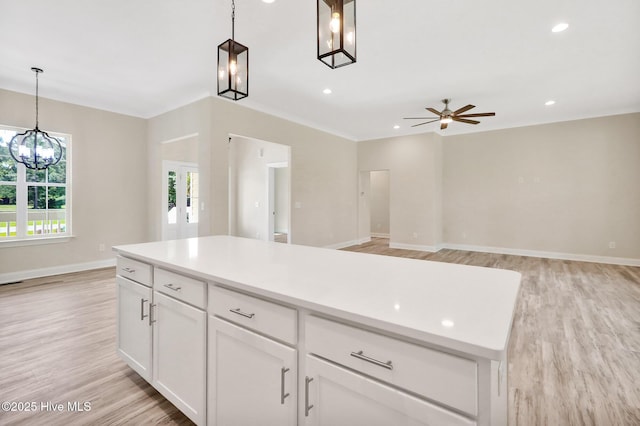kitchen with white cabinets, light wood-type flooring, baseboards, hanging light fixtures, and ceiling fan with notable chandelier