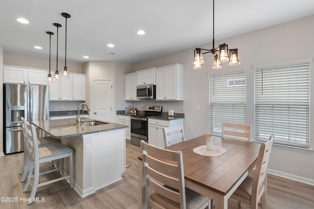 kitchen with white cabinets, sink, an island with sink, appliances with stainless steel finishes, and decorative light fixtures