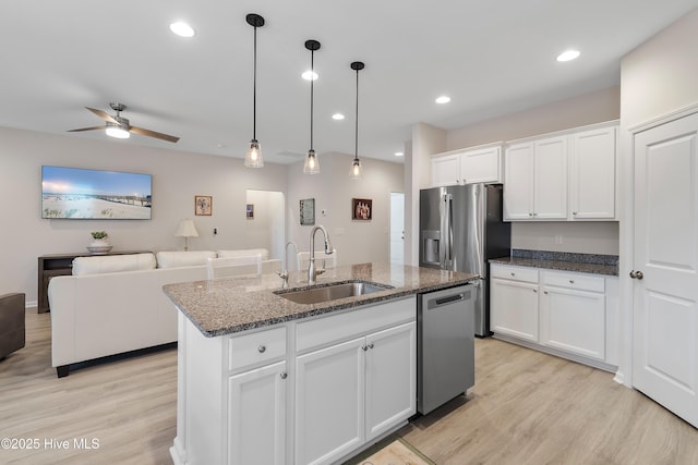 kitchen featuring sink, hanging light fixtures, stainless steel appliances, a center island with sink, and white cabinets