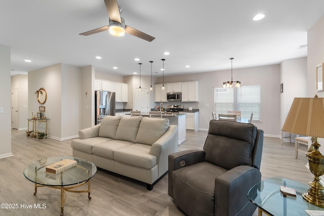 living room featuring ceiling fan with notable chandelier and light wood-type flooring