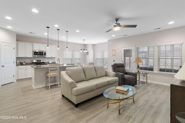 living room featuring ceiling fan with notable chandelier and light hardwood / wood-style flooring