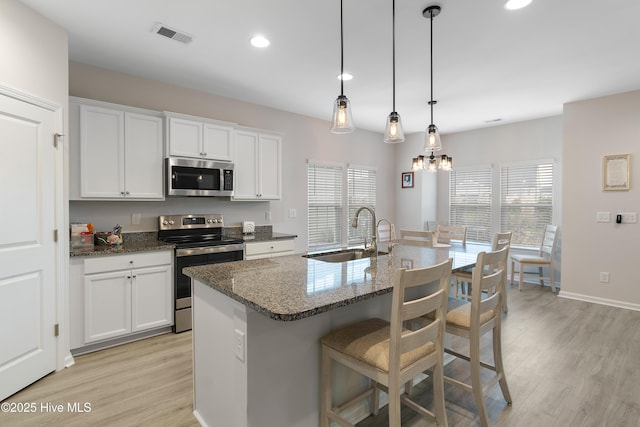 kitchen featuring stainless steel appliances, sink, a center island with sink, dark stone countertops, and white cabinetry