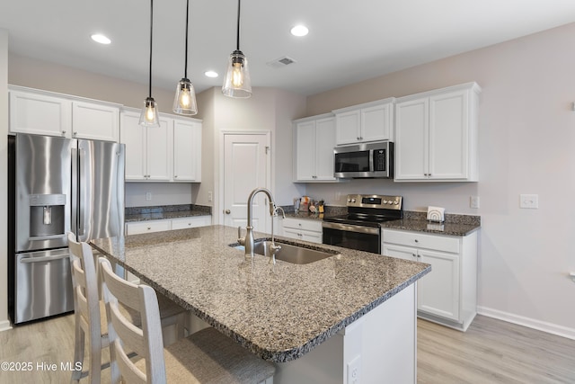 kitchen with stainless steel appliances, sink, dark stone countertops, white cabinets, and an island with sink