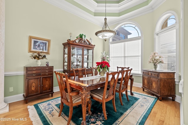 dining room with a raised ceiling, light wood-type flooring, and crown molding