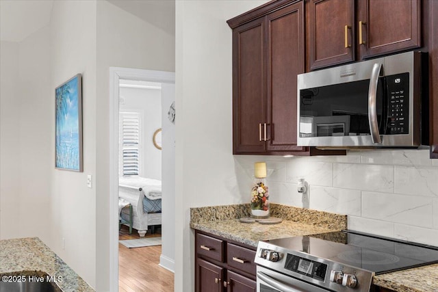 kitchen with light stone countertops, decorative backsplash, appliances with stainless steel finishes, and light wood-type flooring