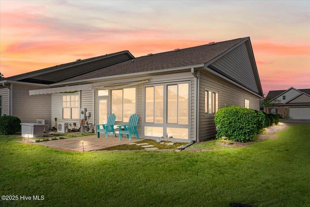 back of property at dusk featuring a patio, a shingled roof, and a yard