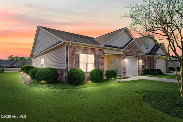 ranch-style house with a garage, driveway, brick siding, a shingled roof, and a yard