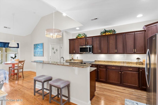 kitchen with appliances with stainless steel finishes, a kitchen island with sink, decorative light fixtures, light stone countertops, and a breakfast bar